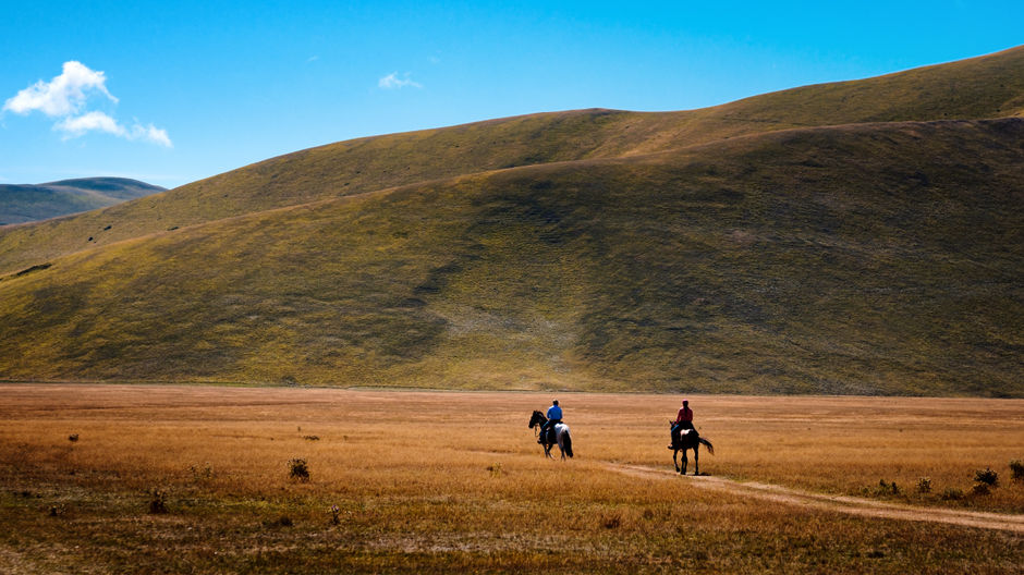 A couple of people riding horses across a dry grass field