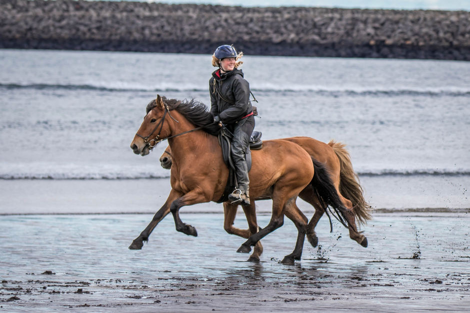 Woman rides a horse on the volcanic sand of the beach