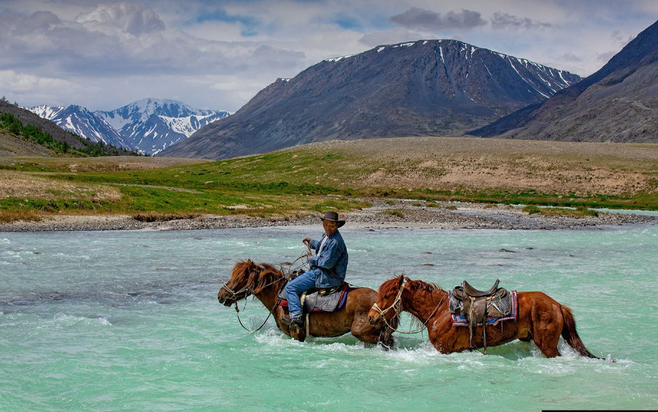 Man on horseback crosses a river in the Altai mountains